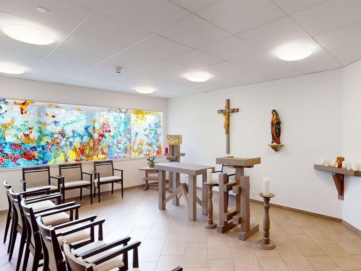 Kapelle mit Stühlen, Wanddeko und bunten Fensterelementen