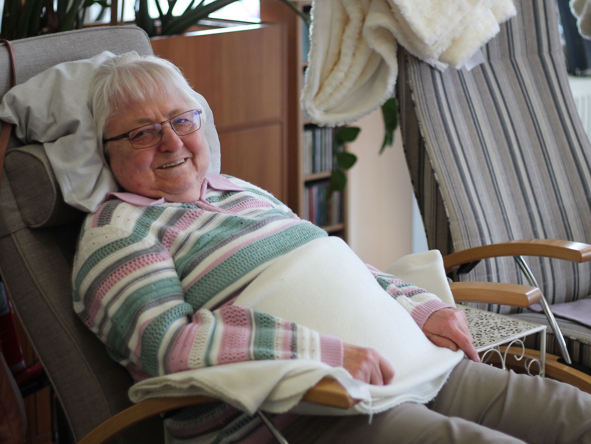 Ältere Dame liegt im Sessel und lächelt in die Kamera.