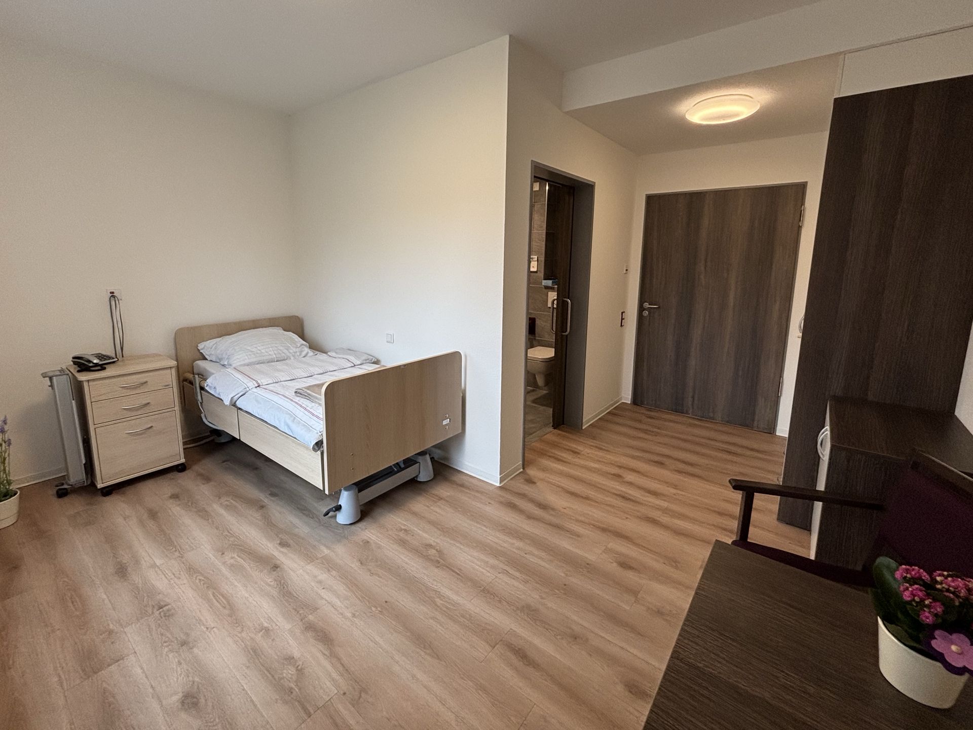 Bewohnerzimmer im Weitwinkel mit Pflegebett und Nachtschrank
