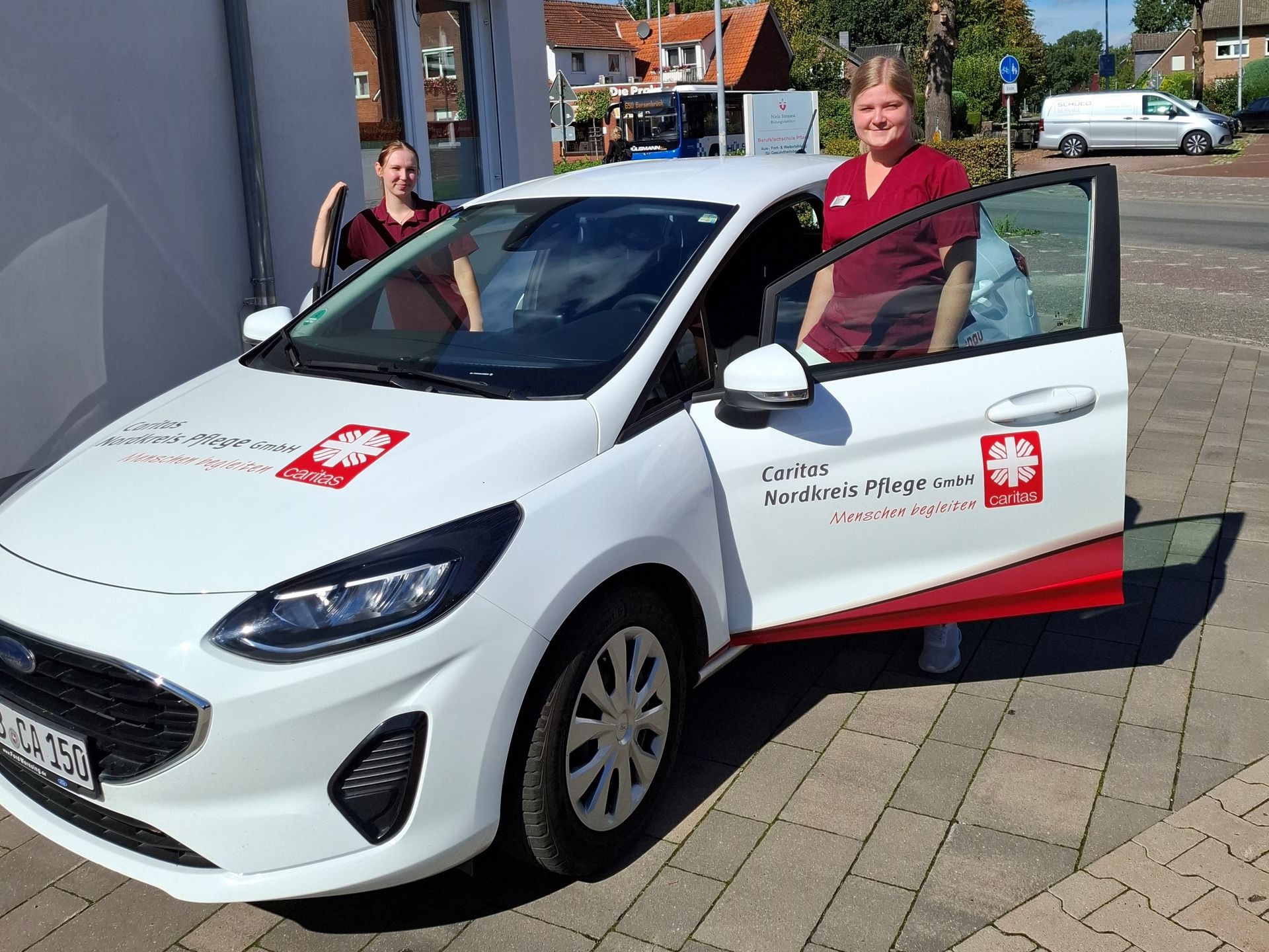 Zwei Frauen stehen an einem weißen Auto und schauen in die Kamera