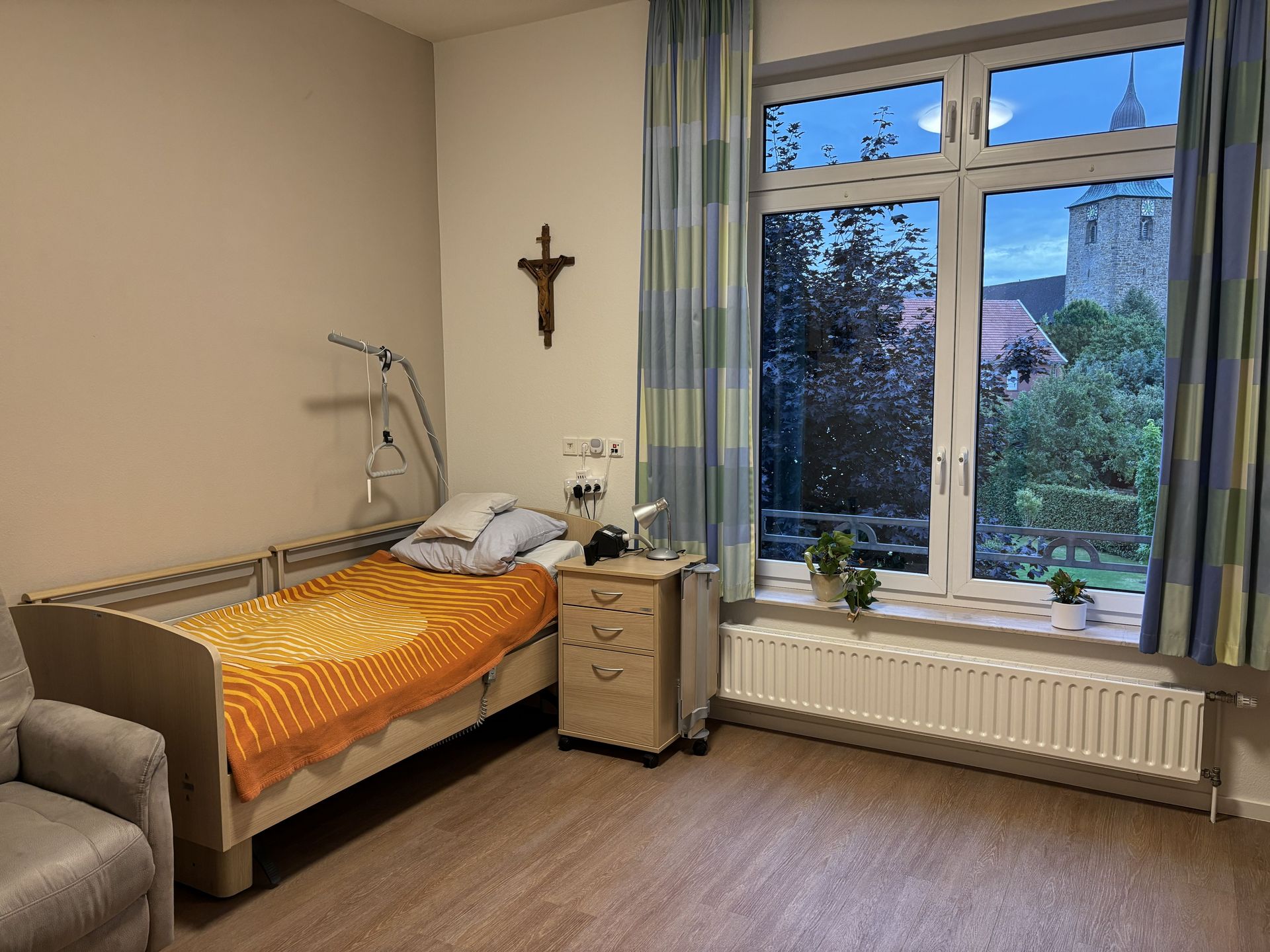 Bewohnerzimmer mit Pflegebett, Nachtschrank und Fenster