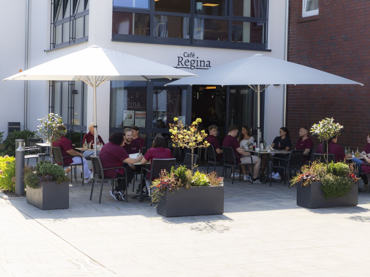 Vor einem Café sind Sonnenschirme aufgespannt unter denen Personen sitzen, die Kaffee trinken