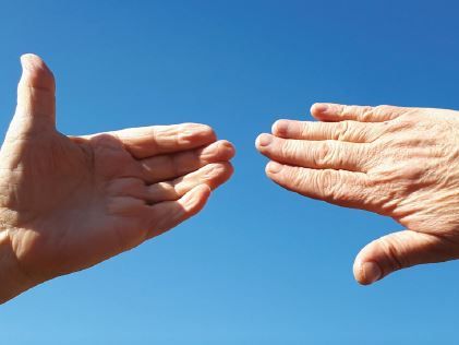 Zwei Hände vor blauem Hintergrund die sich entgegenstrecken aber nicht berühren