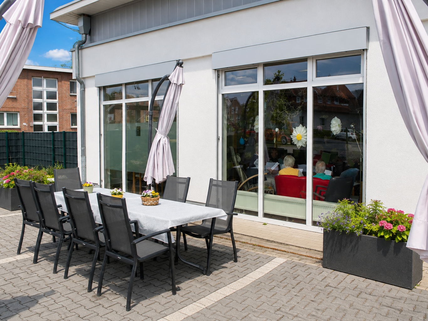 Terrasse mit Stühlen und Tisch. Sonnenschirmen und Blumen.