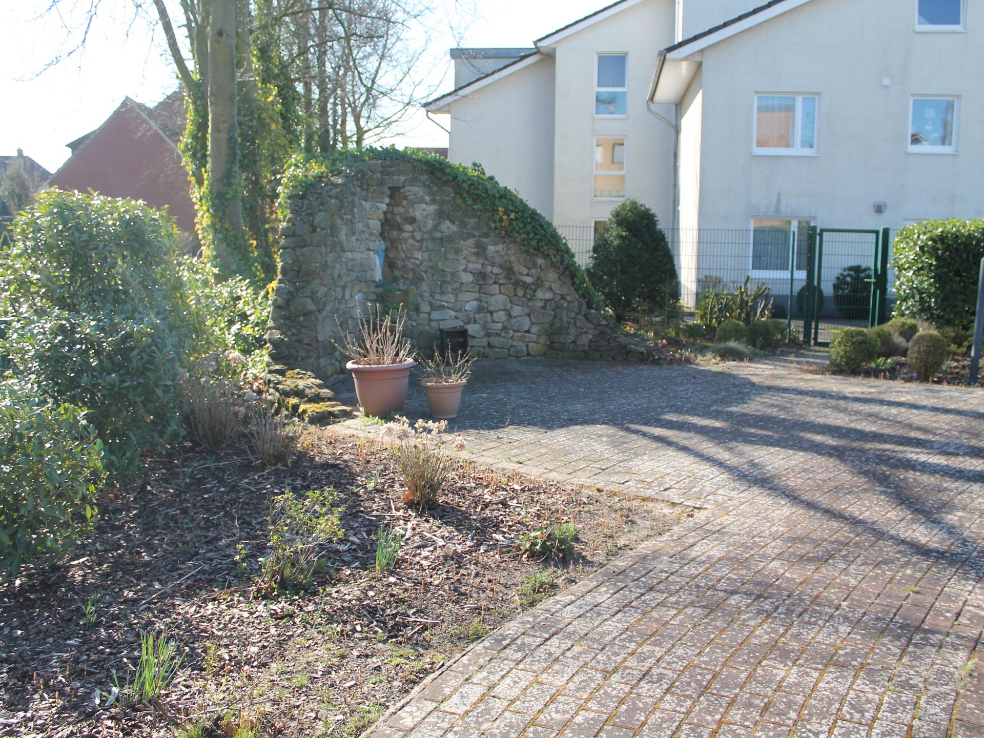 Im Garten. Im Hintergrund Steinmauer. Büsche und Bäume.
