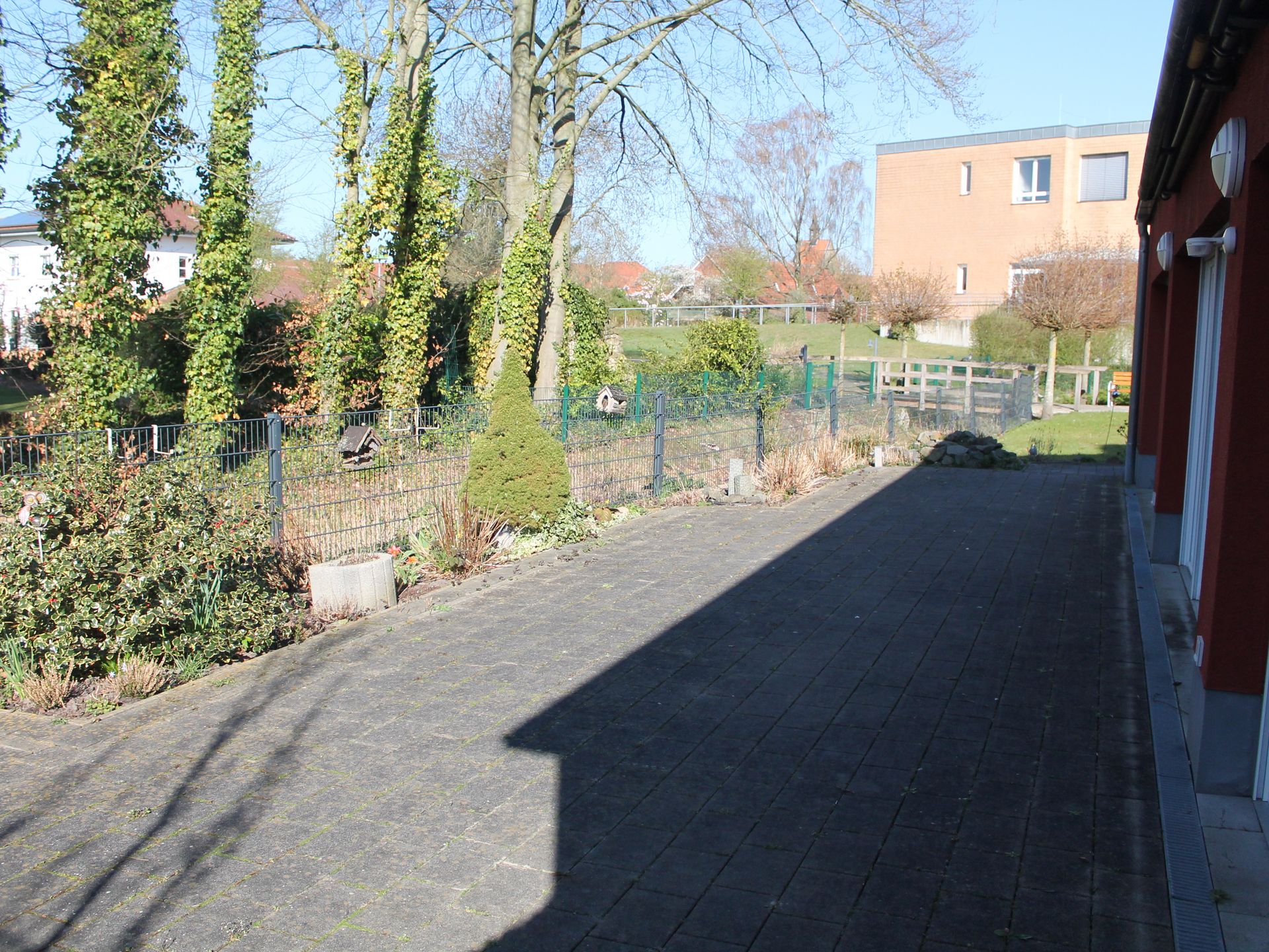 Terrasse. Grau gepflastert. Im Hintergrund Büsche und Bäume.