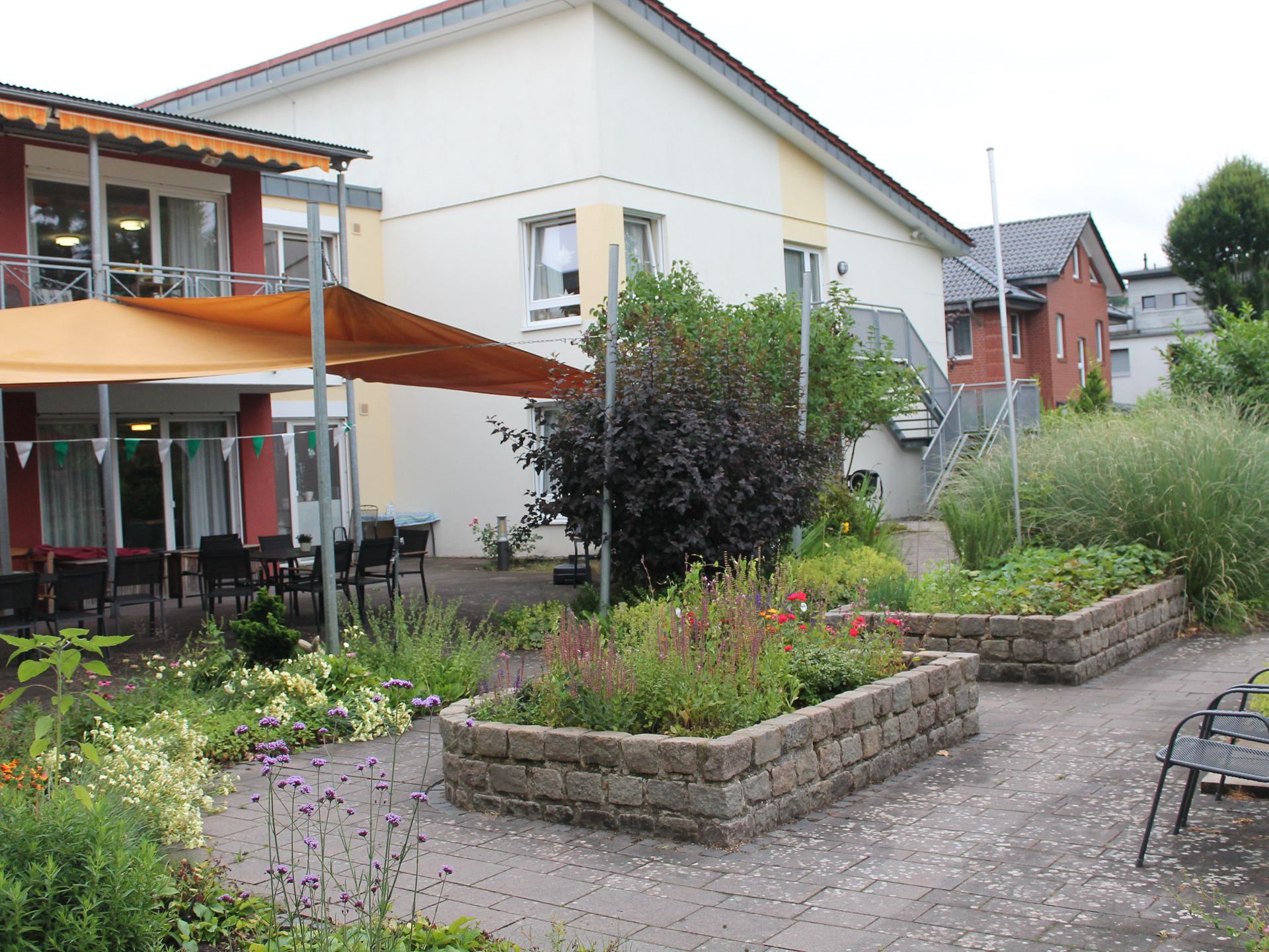Ansicht auf den Außenbereich des Altenheims. Kleiner Garten mit Beeten und Wegen. 