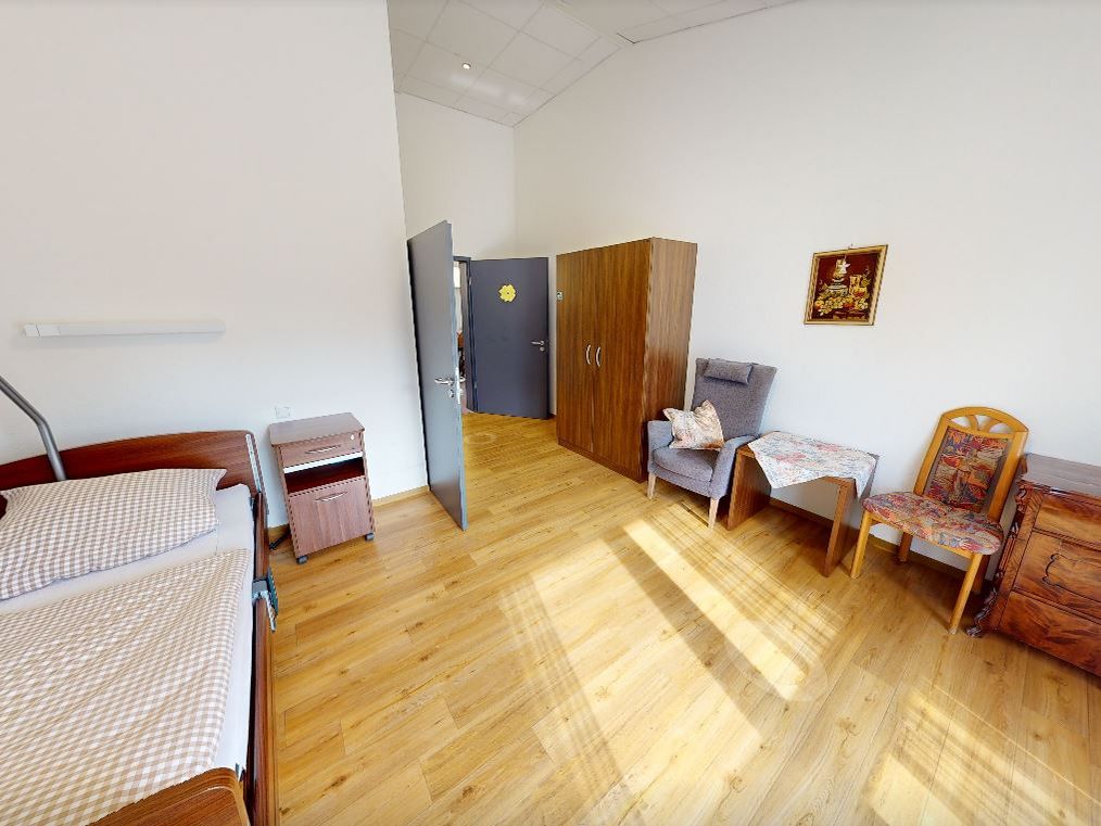 Bewohnerzimmer mit Bett, Nachtschrank und weiteren Möbeln