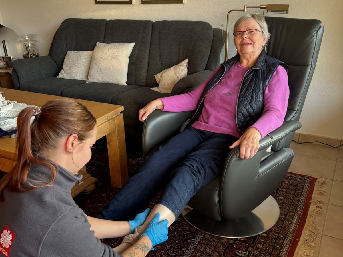 Pflegekraft zieht Oma Strümpfe an. Oma sitzt im Sessel